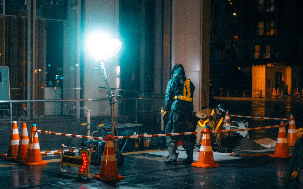 A crew working a site at night under a floodlight, the shift that earns the after-hours rate.