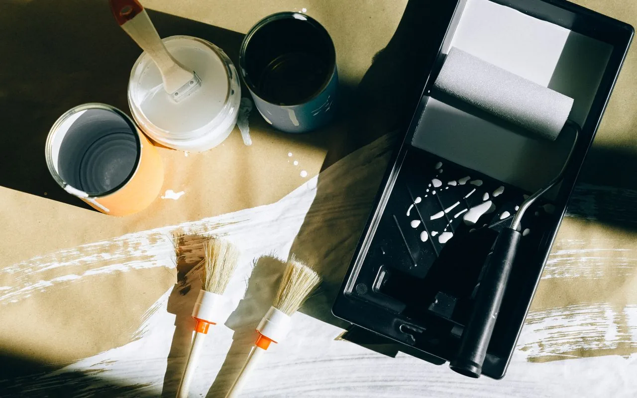 Paint tins, brushes and a roller tray on a drop sheet — the real cost lines behind a round-number prelim.