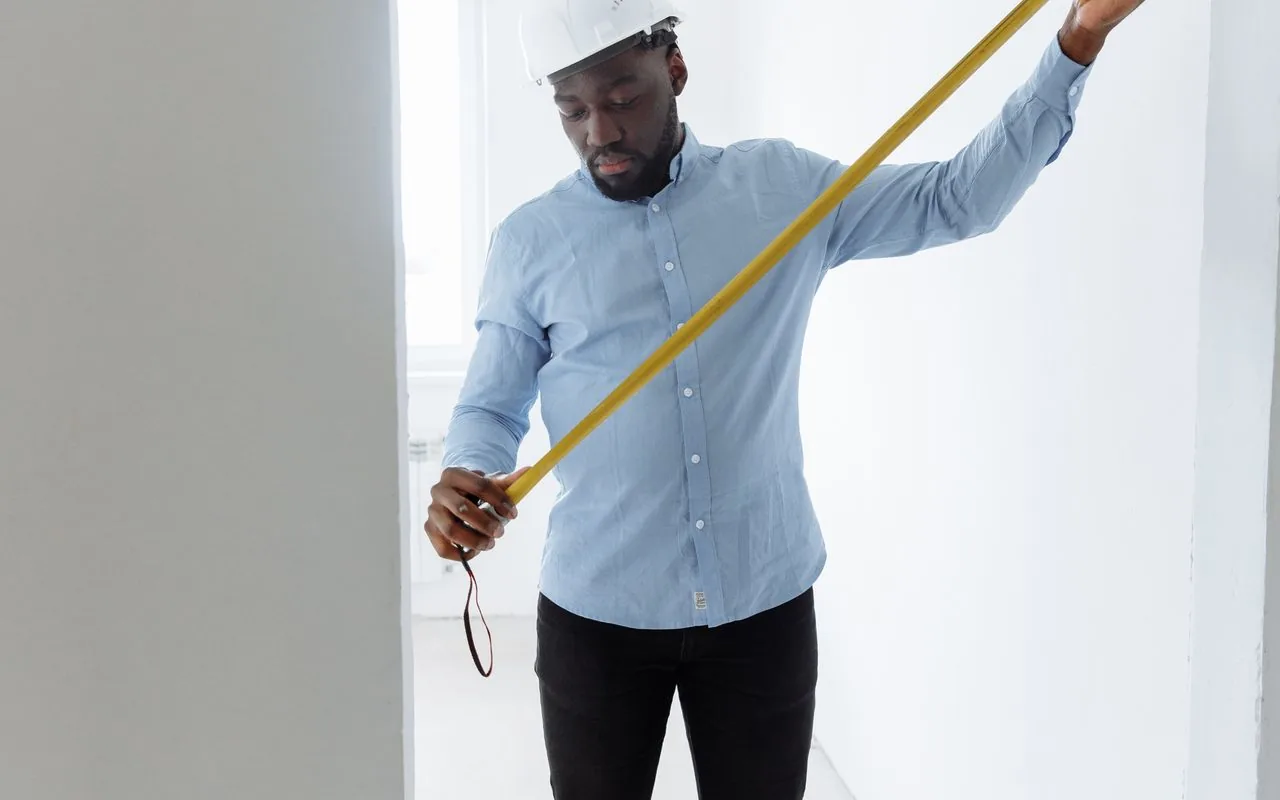 An estimator measuring a wall with a tape: measure first, quote second.