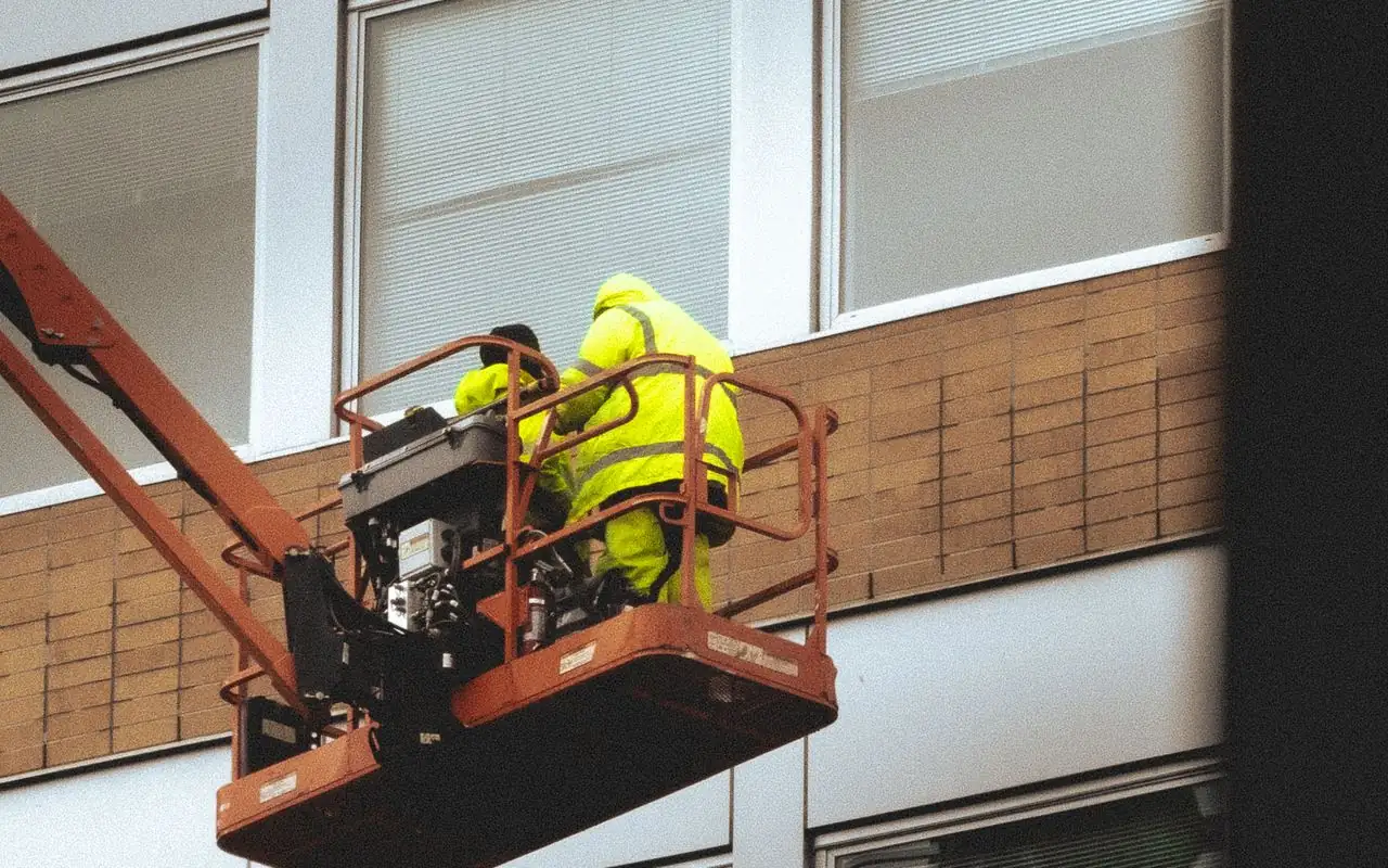 A crew in high-visibility gear working from a boom lift on a commercial facade, the scale of job that gets paid by progress claim.