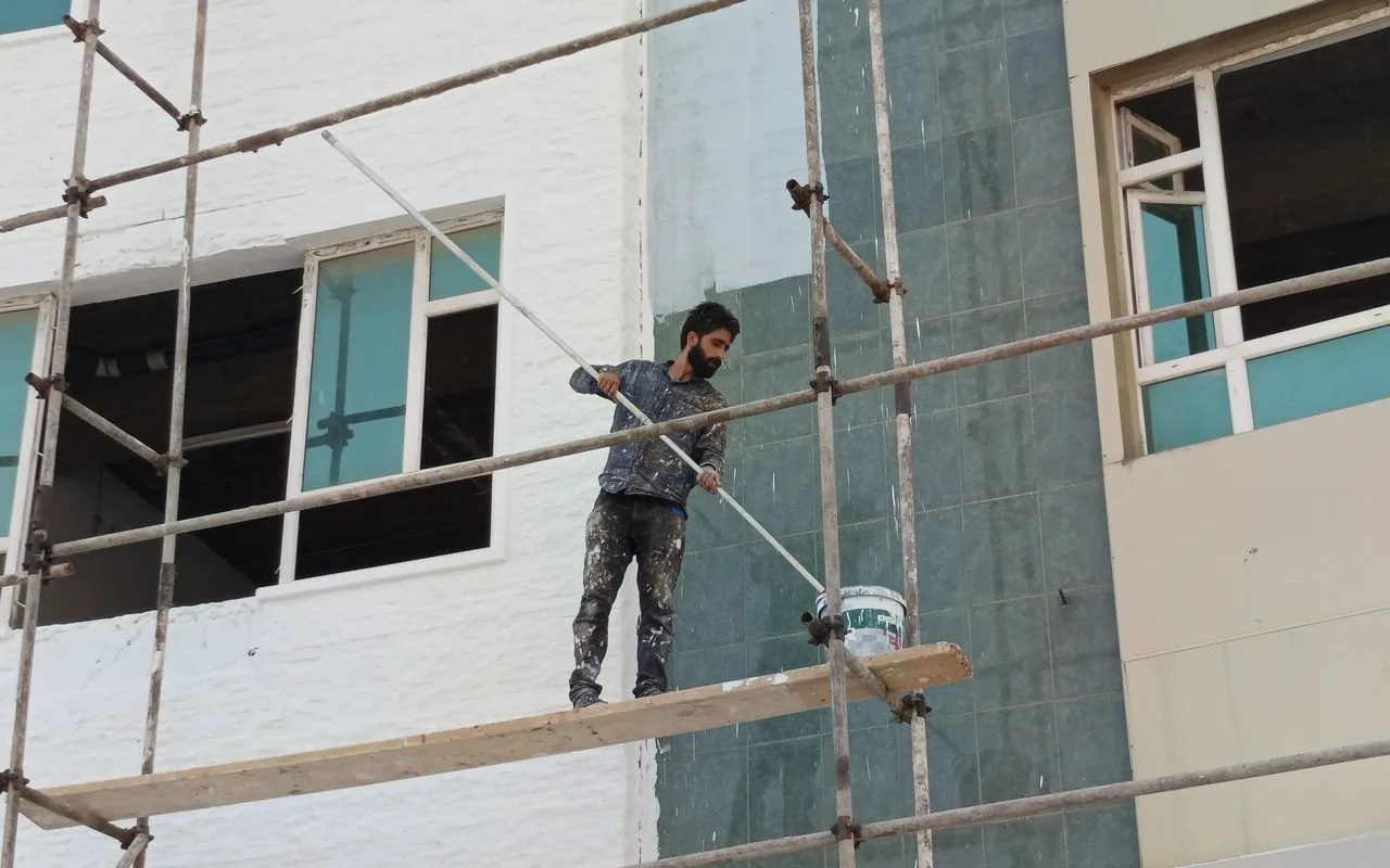 A painter working from scaffolding on a facade — access equipment that has to be priced at quote time, not discovered mid-job.