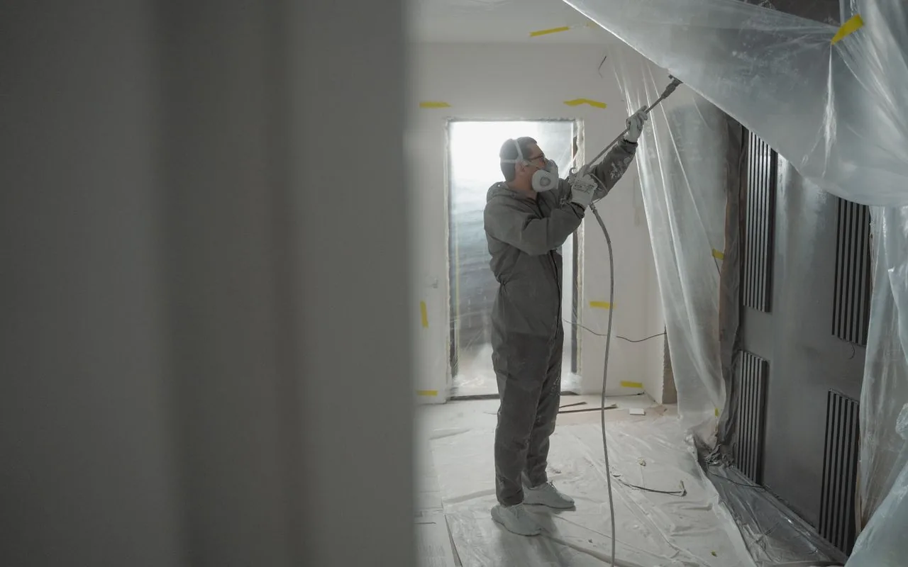 Spraying a room draped in plastic sheeting: the masking is the cost that makes spray slower than it looks.